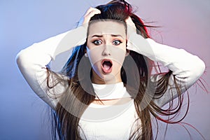 Portrait of a beautiful shocked girl with long hair on studio background, a young woman opened her mouth in surprise, concept