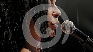 Portrait of a beautiful singer with long hair on a dark stage in the spotlight.