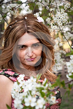 Portrait of beautiful skeptical woman with long hair between blooming with white flowers branches