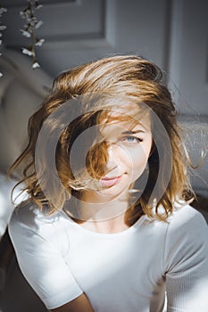 Portrait of a beautiful slim cute girl on a bed with white linen in white top blond wake up and stretches and smiles