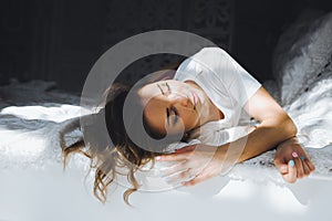 Portrait of a beautiful slim cute girl on a bed with white linen in white top blond wake up and stretches and smiles