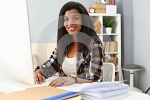 Portrait of beautiful smiling african american office worker sitting at desk and using computer