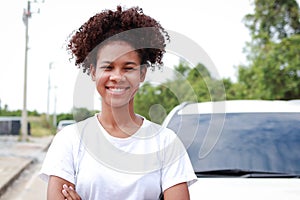 Portrait of a beautiful smiling African American woman standing in front of a car with arms crossed.