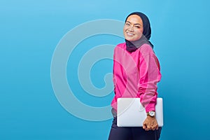 Portrait of beautiful smiling Asian Muslim college student wearing pink sweater holding laptop