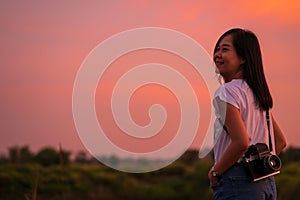 Portrait of beautiful smiling asian woman with holding medium format film camera with colorful sunset sky background