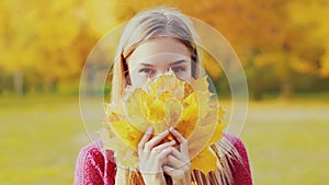 Portrait of beautiful smiling blonde woman with yellow maple leaves in autumn