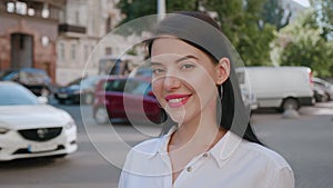 Portrait of beautiful smiling brunette woman on a city background. Young successful businesswoman looks at the camera on