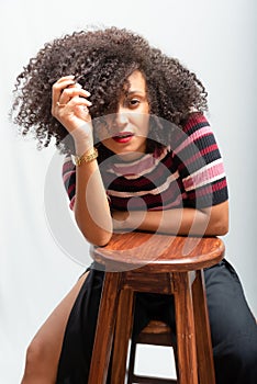 Portrait of a beautiful smiling cheerful young woman with curly hair sitting on a wooden stool
