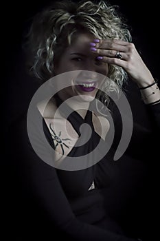 Portrait of a beautiful smiling curly blonde woman who hides from the light with her hand