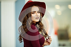 Portrait of beautiful smiling elegant woman is wearing fashion autumn red clothes and hat infront of shop-window