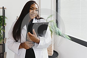 Portrait of beautiful smiling female african american doctor standing in medical office. Health care concept, medical