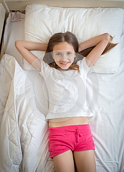 Portrait of beautiful smiling girl in pajamas lying on bed and looking up