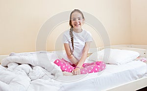 Portrait of beautiful smiling girl in pajamas sitting on bed