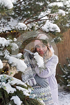 Portrait of a beautiful smiling girl in a pink hat and scarf near a pine branch