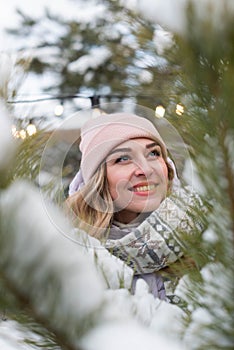 Portrait of a beautiful smiling girl in a pink hat and scarf near a pine branch