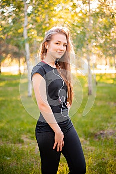 Portrait of a beautiful smiling girl in a sports uniform with flowing hair listening to music in headphones