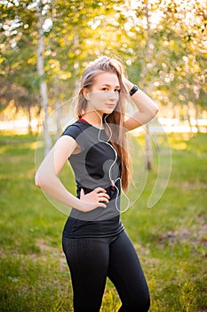 Portrait of a beautiful smiling girl in a sports uniform with flowing hair listening to music in headphones