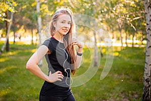 Portrait of a beautiful smiling girl in a sports uniform with flowing hair listening to music in headphones