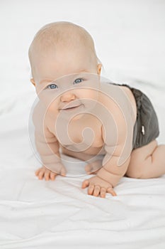 Portrait of beautiful smiling grey-eyed plump cherubic baby infant toddler wearing grey pants standing on all fours.