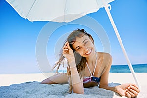 Portrait of beautiful smiling happy woman tanning in sunglasses on sandy beach at summer. Summer vacation concept.