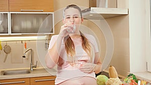 Portrait of beautiful smiling pregnant woman drinking vitamins in pills with clear water. Concept of healthy lifestyle