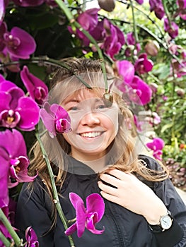 Portrait of the beautiful smiling woman with the blond hair posing in the pink orchids
