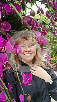 Portrait of the beautiful smiling woman with the blond hair posing in the pink orchids