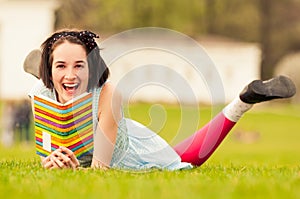 Portrait of beautiful smiling woman lying on grass reading book