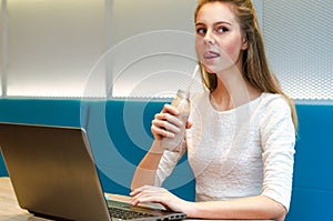 Portrait of beautiful smiling woman sitting on a comfortable chair in a cafe with black laptop. Pretty student doing work with lap