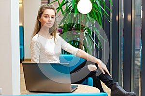 Portrait of beautiful smiling woman sitting on a comfortable chair in a cafe with black laptop. Pretty student doing work with lap