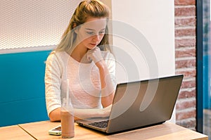 Portrait of beautiful smiling woman sitting on a comfortable chair in a cafe with black laptop. Pretty student doing work with lap