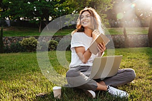 Portrait of beautiful smiling woman sitting on green grass in pa