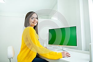Portrait of a beautiful smiling woman, working at the computer with green screen, in an office environment