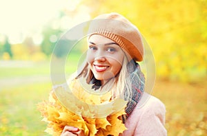 Portrait beautiful smiling woman with yellow maple leafs in warm sunny autumn