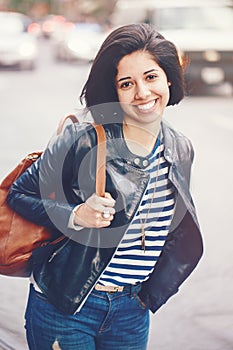 Portrait of beautiful smiling young Caucasian latin girl woman with dark brown eyes, short dark hair, in blue jeans, leather biker