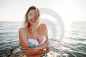 Portrait of beautiful smiling young woman in bikini on beach. Female model posing in swimsuit on sea shore. Summer holidays,