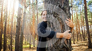 Portrait of beautiful smiling young woman leaning and hugging big old tree in forest. Concept of love, ecology