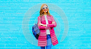 Portrait of beautiful smiling young woman wearing pink jacket on city street on blue background