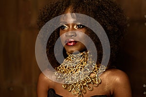 Portrait of beautiful South African young woman with bright red lips wearing gold necklace over bronze wall