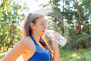 Portrait of beautiful sporty woman drinking water after fitness training in summer park or forest.Closeup.Side view