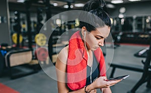 Portrait of a beautiful sporty young woman listening to music from her smartphone, preparing for a hard workout in the gym. People