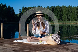 Portrait beautiful stylish romantic retro girl holding flower branch in hand while sitting at pier near the lake