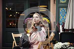 Portrait of beautiful stylish young woman sitting in street cafe . Model looking aside. City lifestyle. Female fashion