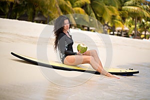 Portrait of a beautiful surfing girl with green coconut from palm tree sit on yellow surf longboard surfboard board.