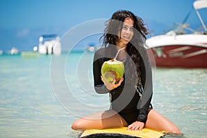 Portrait of a beautiful surfing girl with green coconut from palm tree sit on yellow surf longboard surfboard board.