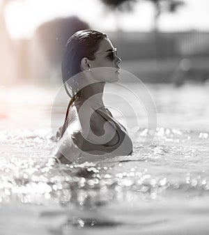 Beautiful tanned woman in blue swimwear relaxing in swimming pool spa near expensive villa on hot summer day