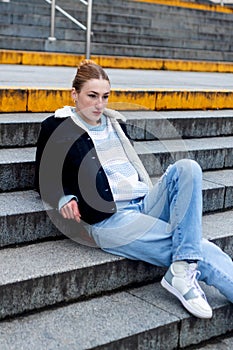 Portrait of a beautiful teen girl sitting on the street. Photos in cold colors
