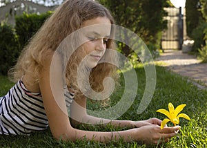 portrait of beautiful teenage girl 12 years old, lying on grass on sunny day, daydreaming, looking at flower in hands