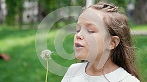 Portrait of a beautiful teenage girl blowing on the ripened dandelion in a spring or summer park. Slow motion video