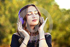 Portrait of a beautiful teenager girl with headphones on head, young woman listening to music on the nature